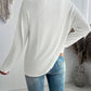 Back view of woman wearing a white textured V-neck long sleeve T-shirt and blue jeans in a casual setting