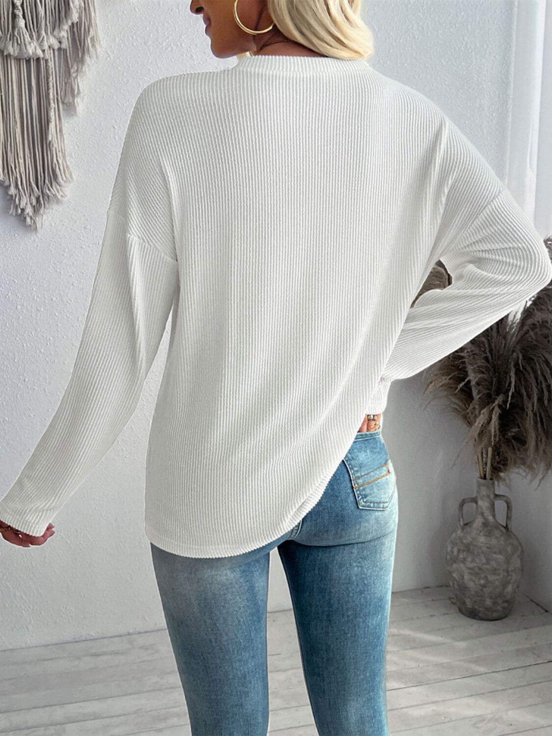 Back view of woman wearing a white textured V-neck long sleeve T-shirt and blue jeans in a casual setting