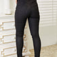 High rise black coated ankle skinny jeans, rear view showing sleek and glossy texture, figure-hugging fit with exposed button closure.