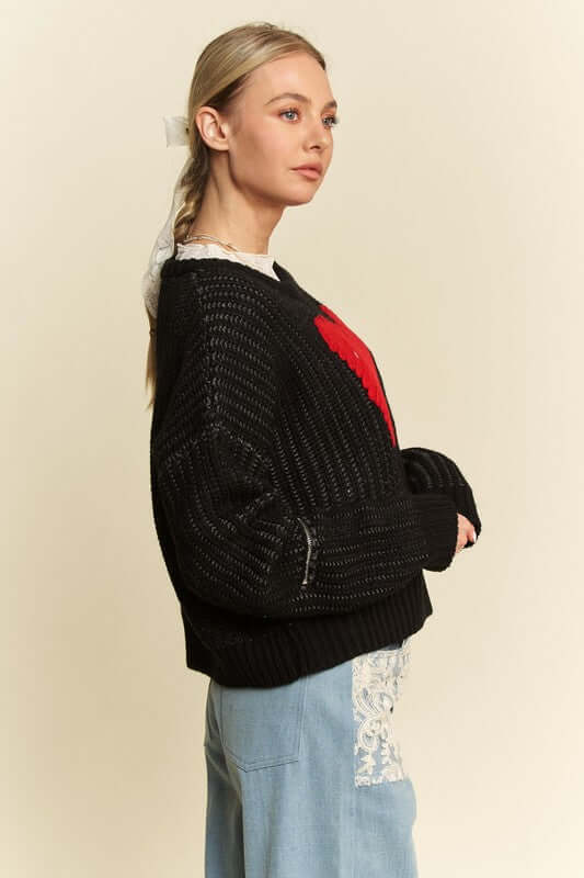 Model showcasing the Davi & Dani Contrast Heart Dropped Shoulder Sweater with a stylish black design and playful red heart.