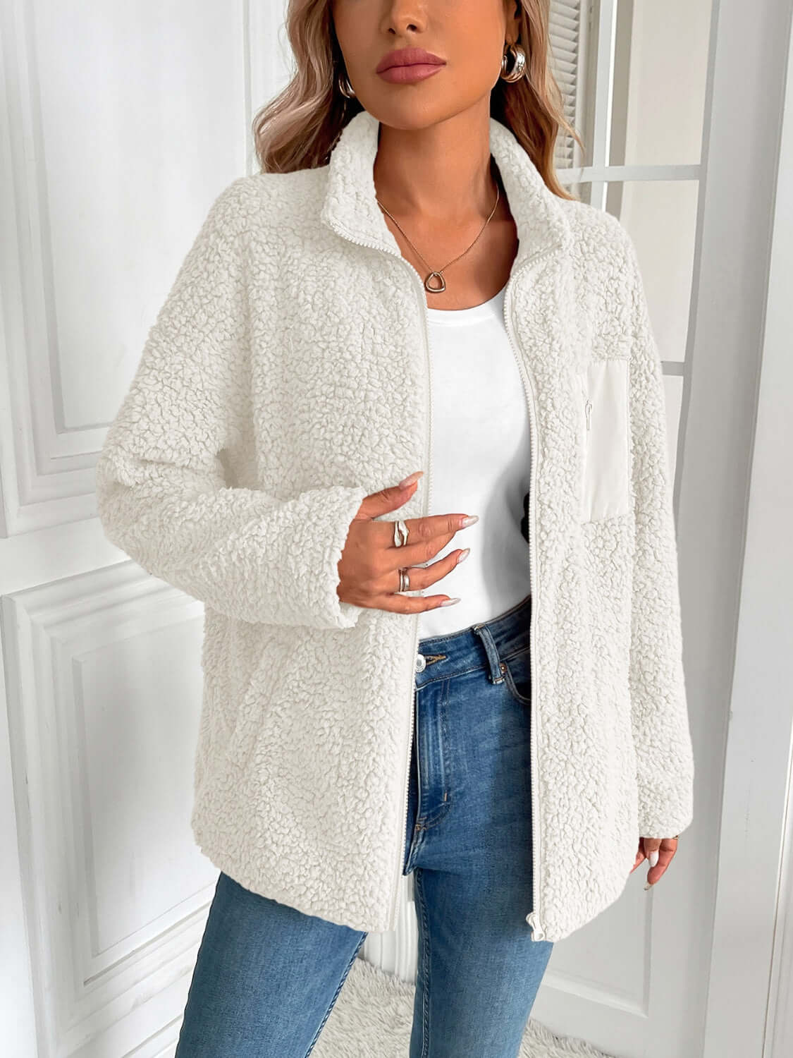 Woman wearing Ivy Lane white fuzzy zip-up jacket with long sleeves and pockets, styled with jeans for a cozy, chic look.