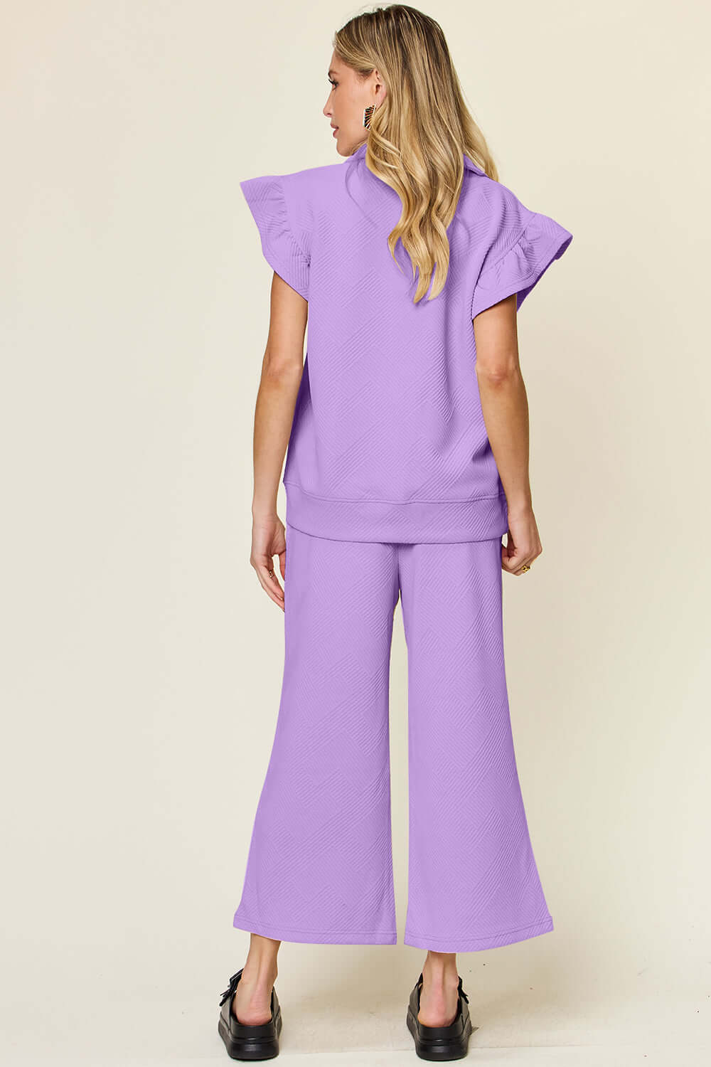 Woman wearing a lavender ruffle short sleeve top with drawstring wide leg pants set, viewed from the back.