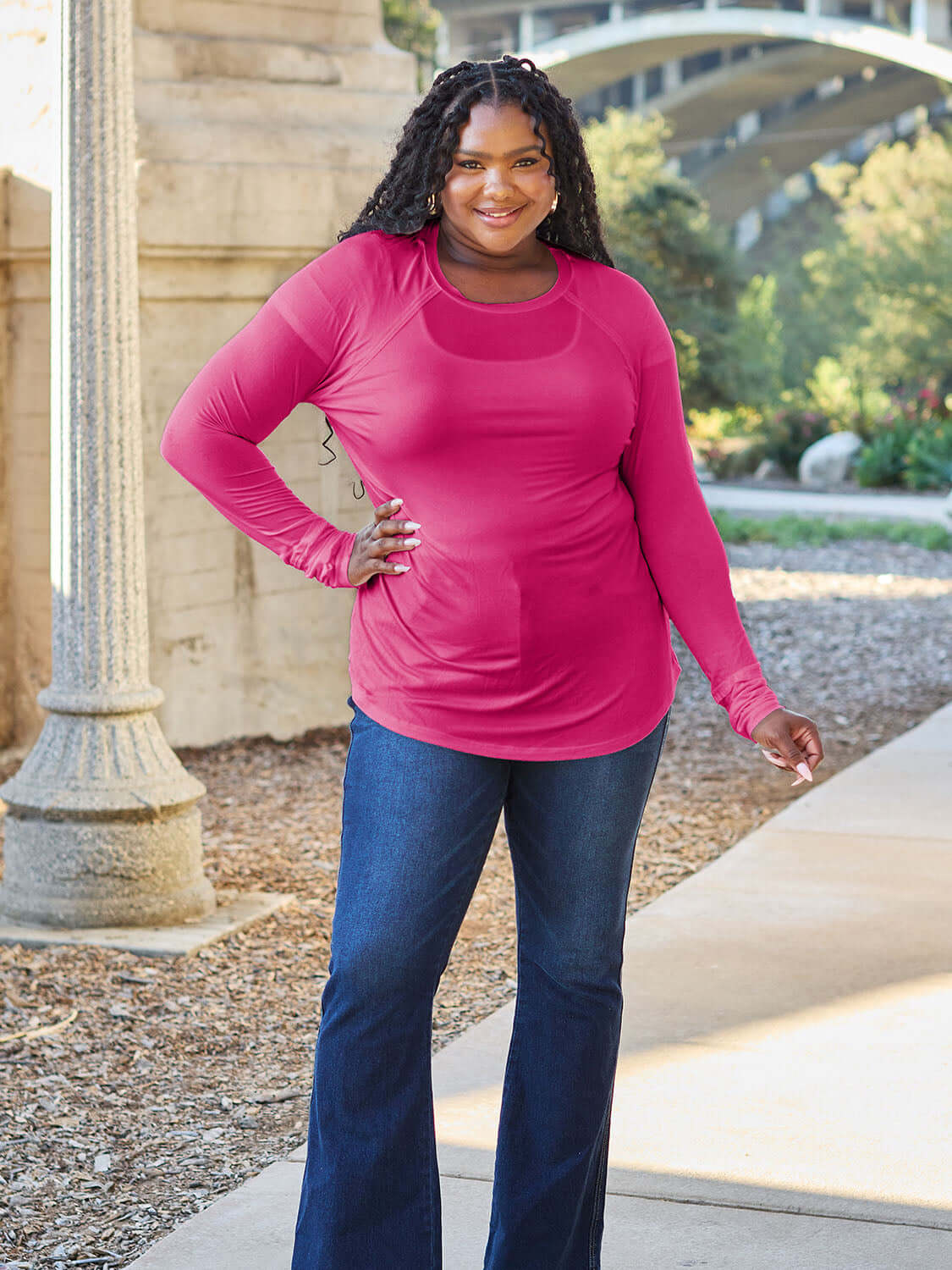 Woman wearing a pink round neck long sleeve t-shirt made of slightly stretchy rayon and spandex, paired with jeans, in an outdoor setting.