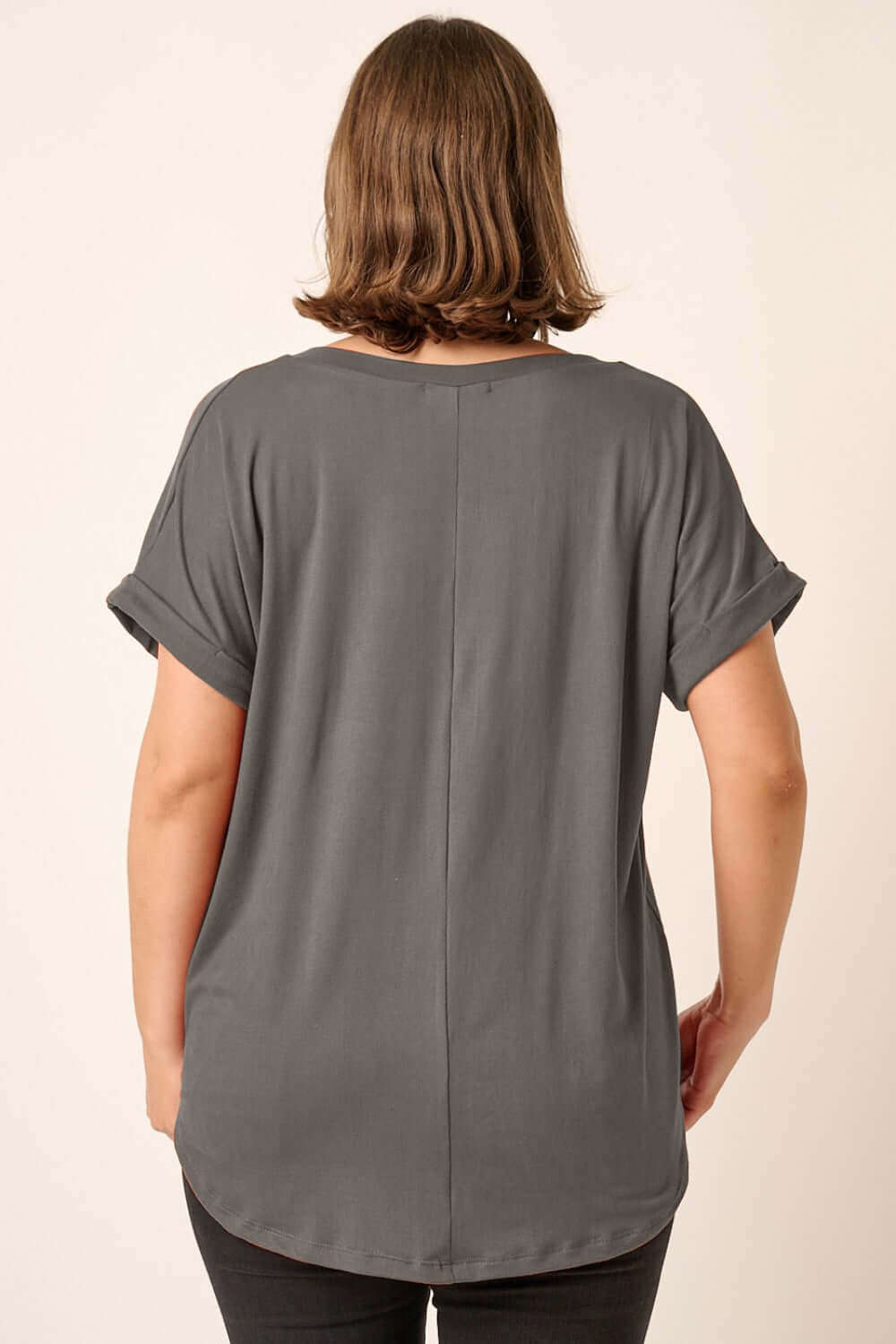 Back view of a woman wearing a grey V-neck rolled short sleeve T-shirt, showcasing the rolled sleeves and relaxed fit.