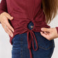 Close-up of drawstring detail on a maroon long sleeve top paired with blue jeans