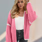 Woman wearing open front pink cardigan with dropped shoulders and white trim, paired with a white top and jeans. Trendy and chic style.