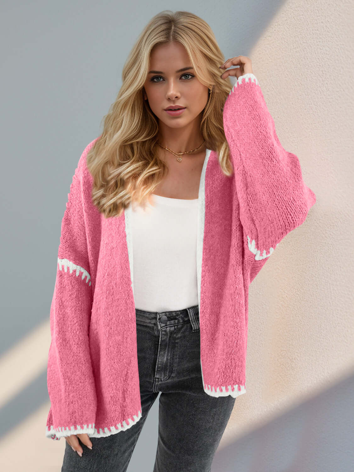 Woman wearing open front pink cardigan with dropped shoulders and white trim, paired with a white top and jeans. Trendy and chic style.