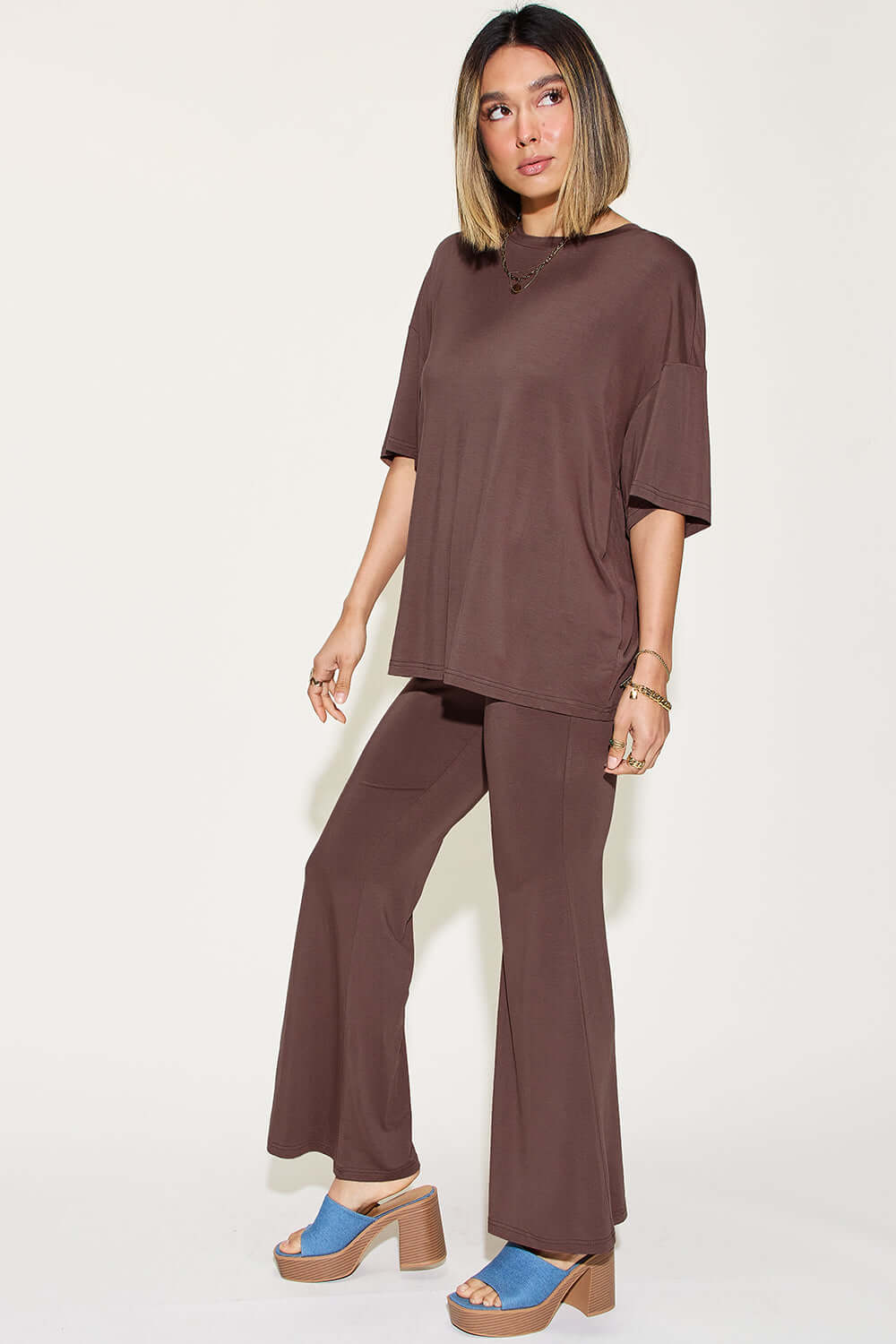 Woman wearing a bamboo drop shoulder T-shirt and flare pants set in brown with blue platform sandals.