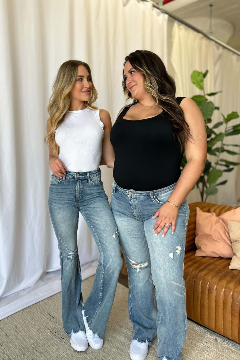 Two women wearing Judy Blue medium rise tummy control destroy flare jeans, showcasing the stylish fit and distressed detailing.