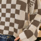 Woman wearing BiBi Checkered Contrast Chunky Sweater with bold checkered design and jeans