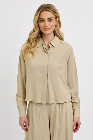 Woman wearing RISEN Button Down Long Sleeve Shirt in beige, featuring a classic design and front pocket.