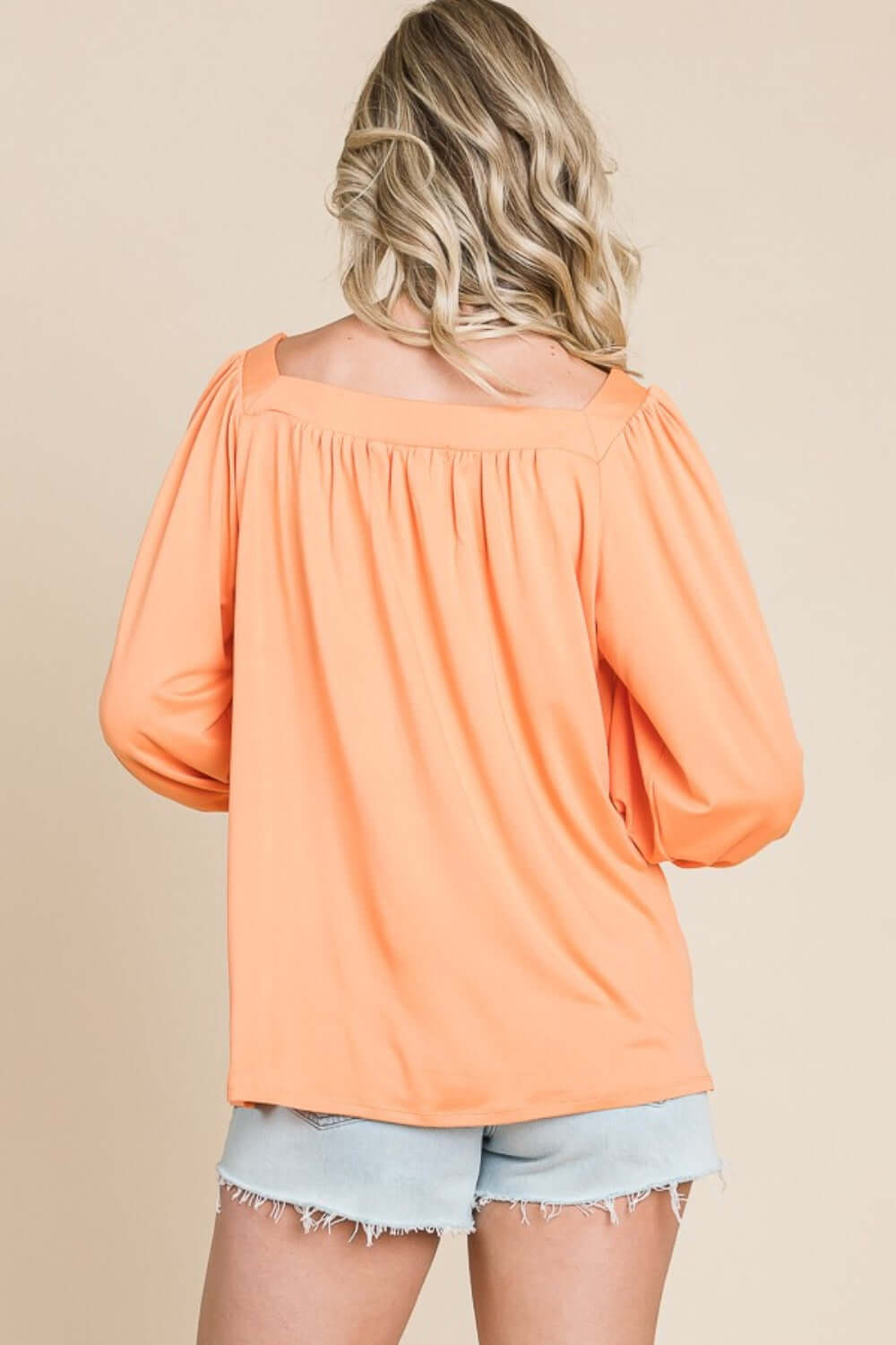 Back view of a woman wearing a trendy Square Neck Puff Sleeve Top in orange paired with light blue denim shorts.