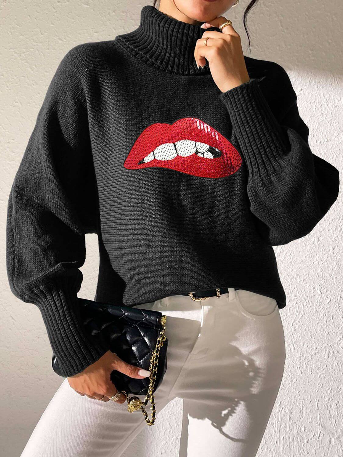 Black Bella Road Lip Turtleneck Sweater with bold red lip design, worn with white pants and black clutch for stylish look