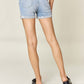 Back view of woman wearing high waist rolled denim shorts from Judy Blue Jeans with a white top and black shoes