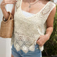 Woman in a crochet cover-up with a tank top and denim shorts, holding a woven bag, enjoying a sunny outdoor setting.