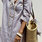 Woman wearing Bella Road Tied Button Up Three-Quarter Sleeve Dress with a striped pattern, accessorized with a woven bag and layered necklaces.