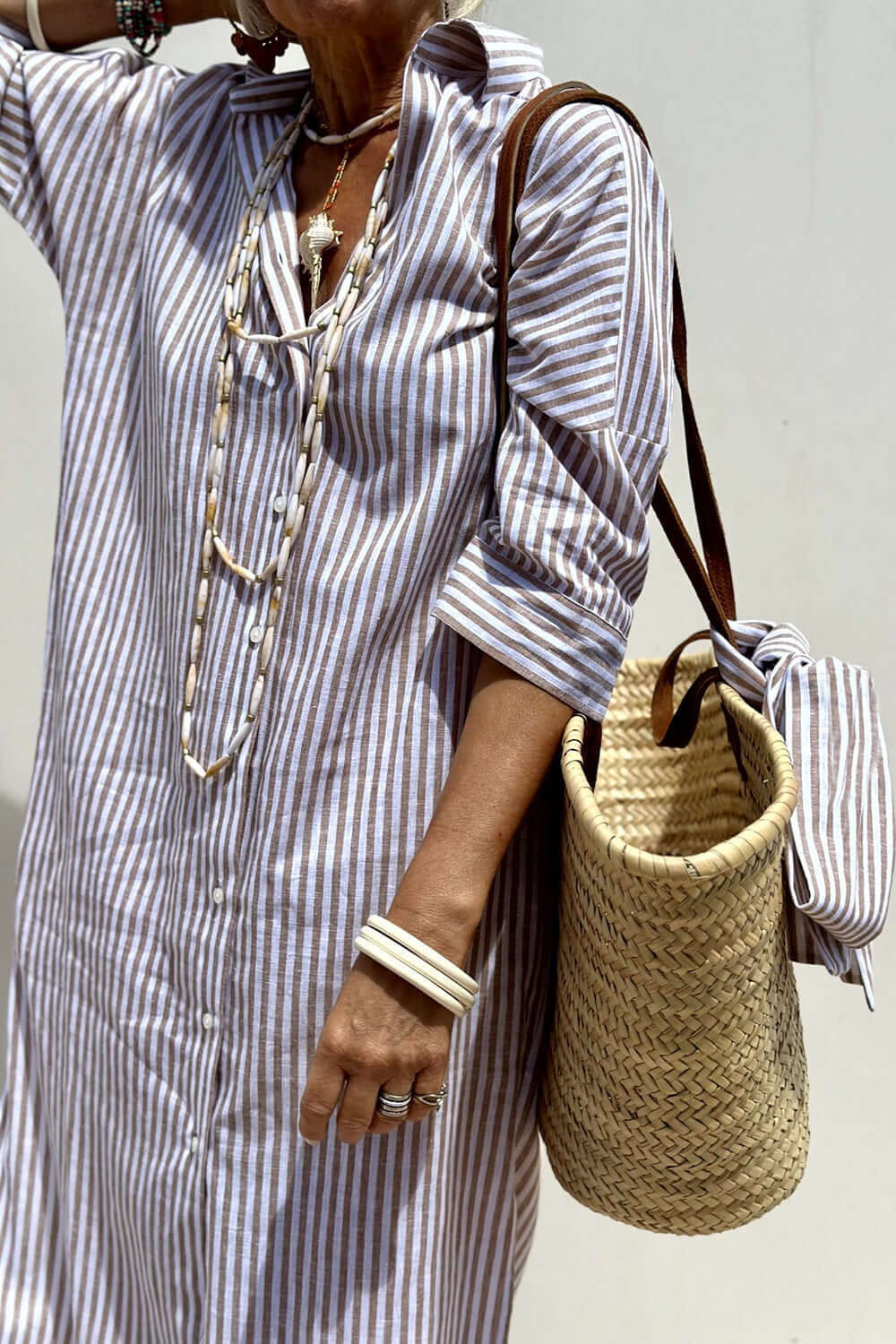 Woman wearing Bella Road Tied Button Up Three-Quarter Sleeve Dress with a striped pattern, accessorized with a woven bag and layered necklaces.