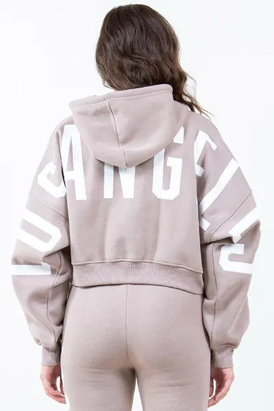 Back view of American Bazi 'Los Angeles' cropped hoodie in light brown with bold lettering and drawstring detail.