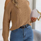 Woman wears Bella Road Cable-Knit Turtleneck Cold Shoulder Sweater with jeans, holding a white clutch. Cozy and trendy fashion style.