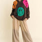 Trendy woman wearing Davi & Dani oversized sweater with colorful smiley faces, styled with relaxed pants for a cozy look.