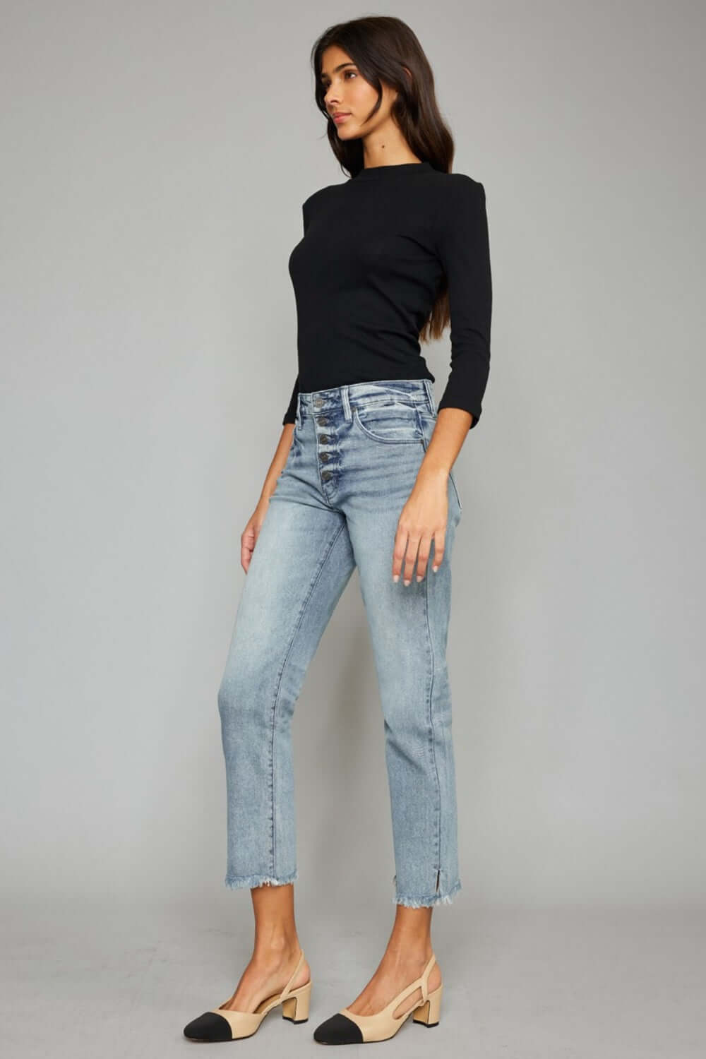 Woman wearing high waist button fly raw hem cropped straight jeans with a black top and beige heels