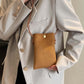 Woman wearing a beige blazer, holding a Bella Road Suede Snap Down Crossbody Bag with a snap-down design and crossbody strap.