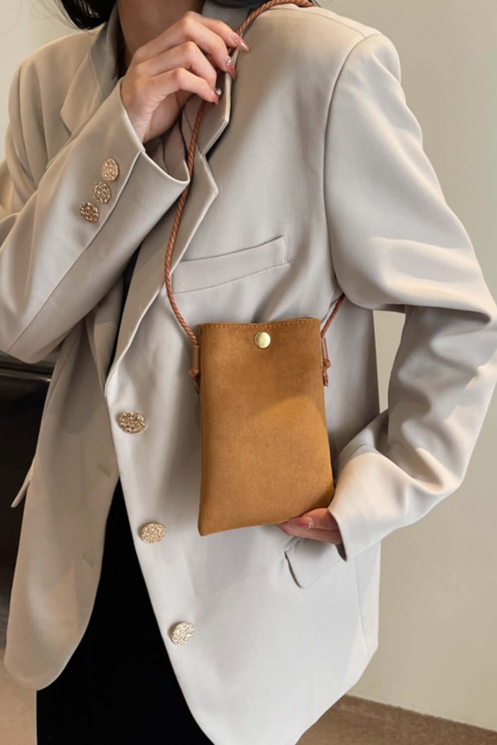 Woman wearing a beige blazer, holding a Bella Road Suede Snap Down Crossbody Bag with a snap-down design and crossbody strap.