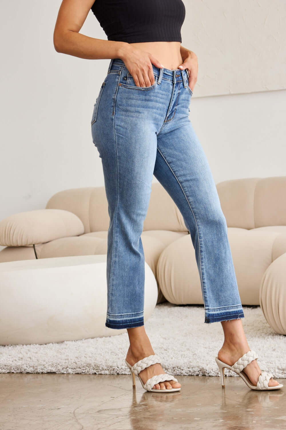 Woman wearing release hem cropped bootcut Judy Blue Jeans with high heels, showcasing trendy and versatile denim style in a modern setting