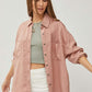 Woman wearing RISEN full-size button-up long sleeve denim shirt in pink, paired with a green crop top and white pants, casual stylish look