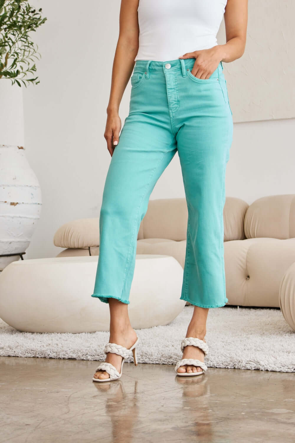 Woman wearing Crop Chloe Full Size Tummy Control High Waist Raw Hem RFM Jeans in aqua paired with white top and sandals