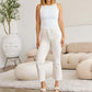 Woman wearing Mini Mia High Waist Raw Hem Jeans in pale color, standing in stylish living room. Perfect jeans for shaping waistline and showing fashion taste.