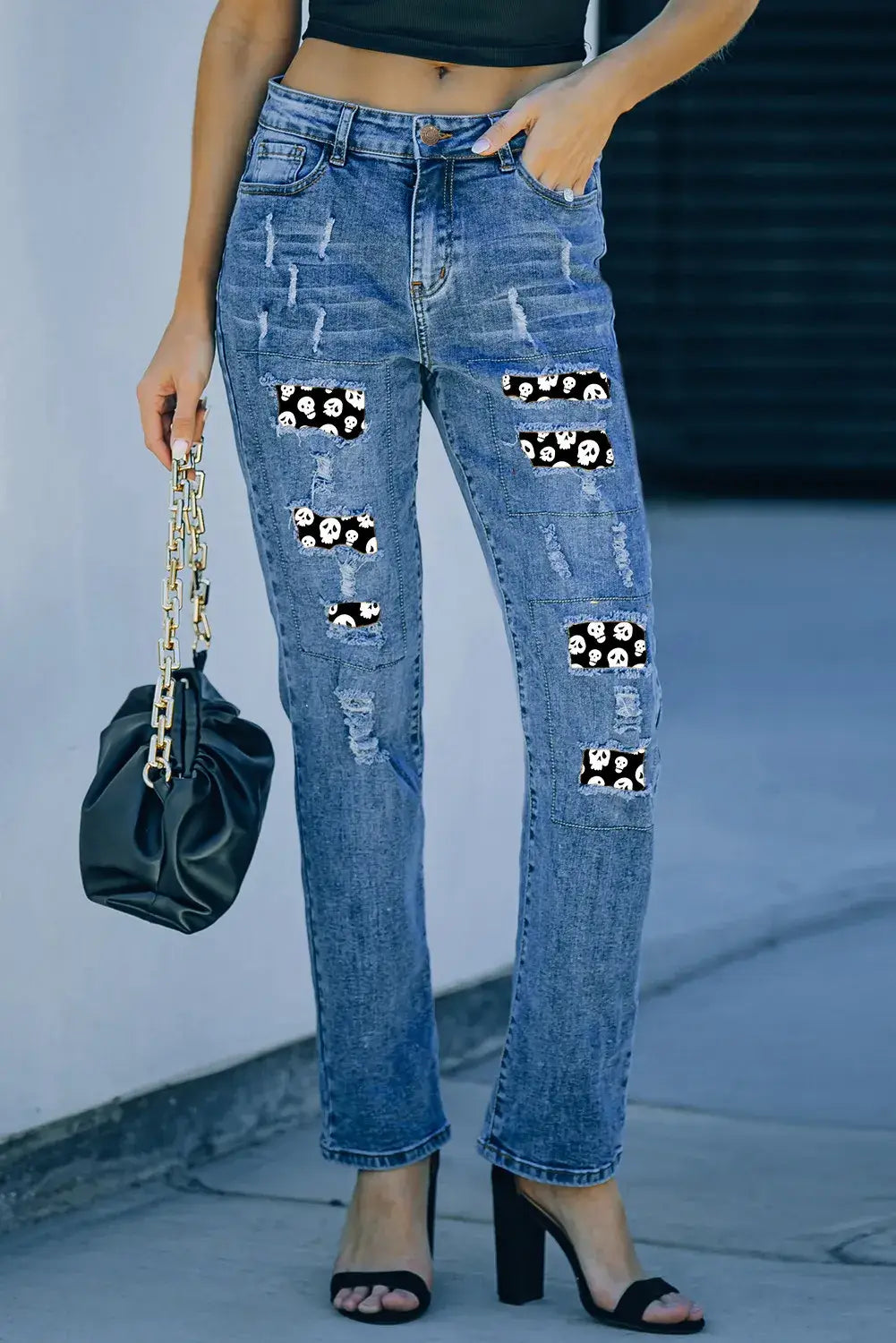 Woman wearing distressed slightly stretchy jeans with skeleton pattern and pockets, holding a black purse.