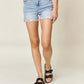 Woman wearing Judy Blue Jeans high-waist rolled denim shorts with a white top and black sandals.