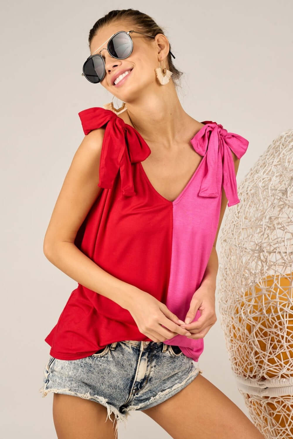 Woman wearing Shoulder Ribbon Tied Contrast Tank with eye-catching red and pink color, paired with denim shorts and sunglasses, stylish fashion look