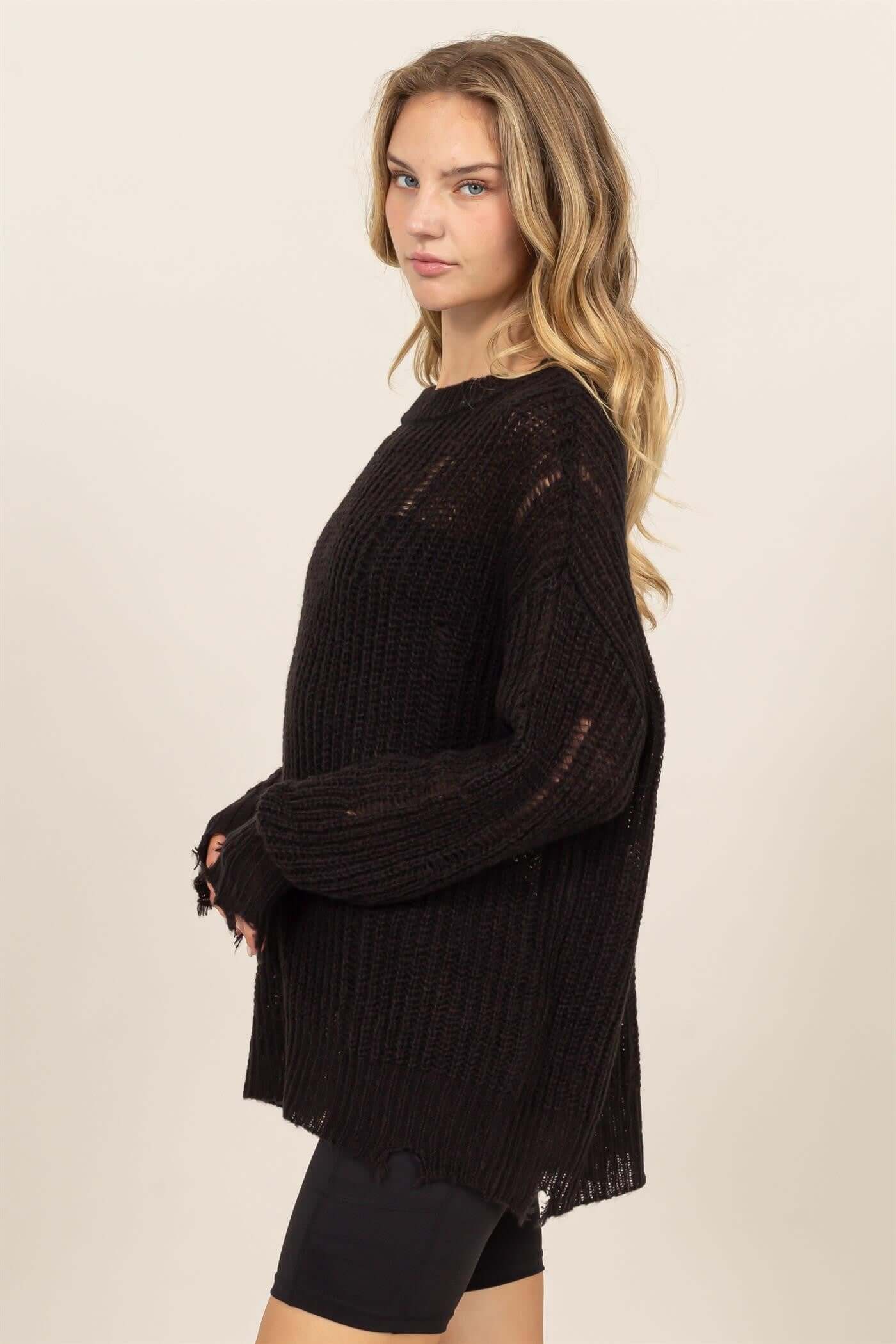 Woman wearing HYFVE distressed long sleeve knit top with crew neck and drop shoulders in black, showcasing chic and relaxed style.