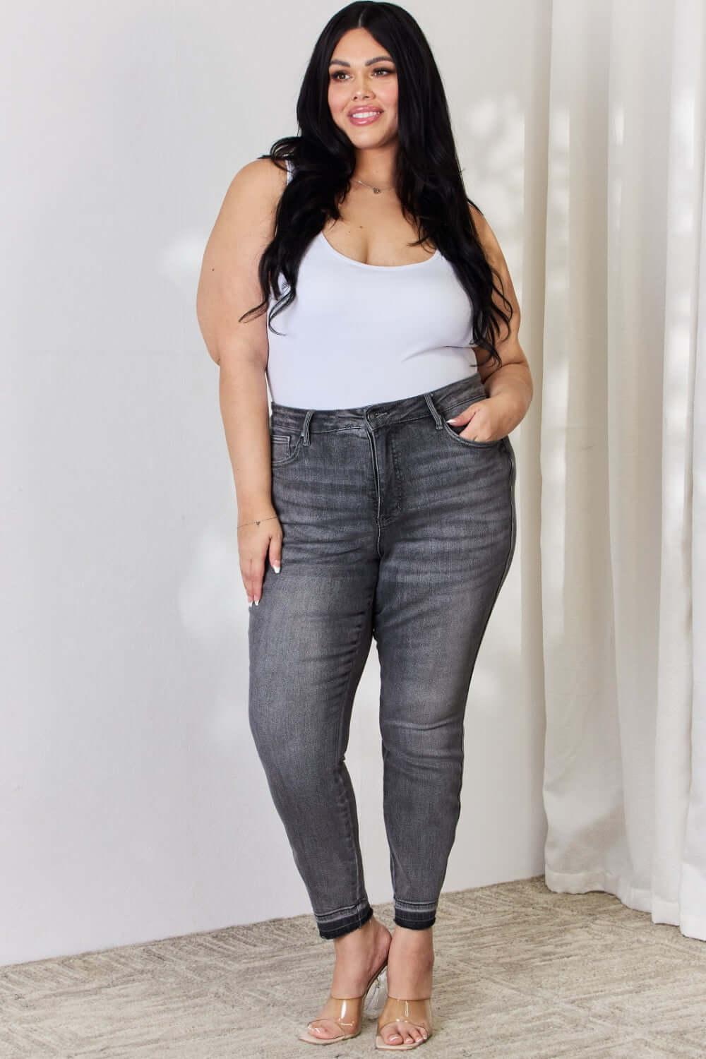 Woman wearing High Waist Tummy Control Release Hem Skinny Jeans in gray by Judy Blue, showcasing flattering silhouette and chic release hem detail