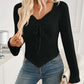 Woman wearing Bella Road ribbed drawstring long sleeve t-shirt in black, paired with jeans and holding a white clutch in a stylish indoor setting.