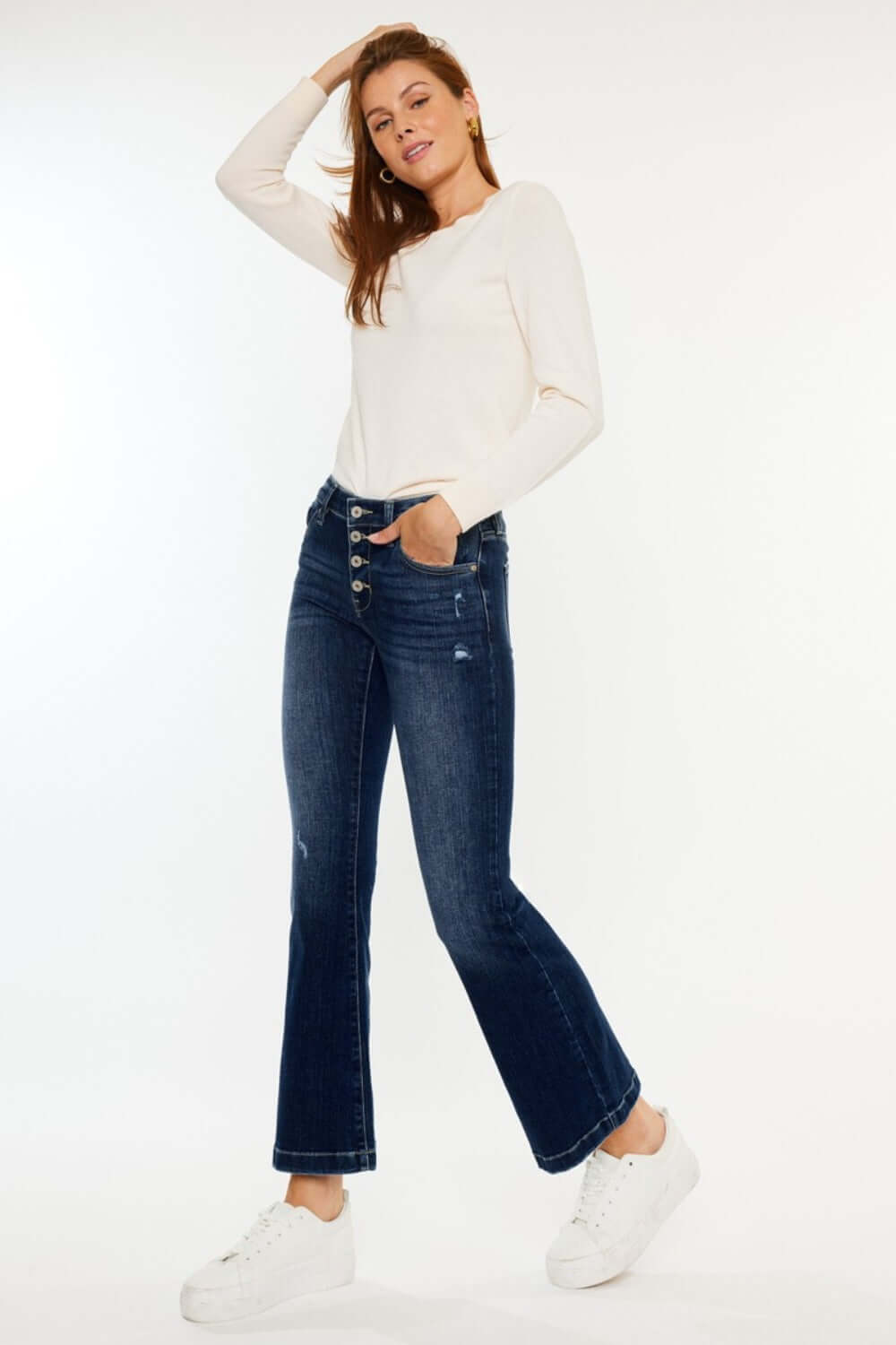 Woman wearing Kancan Mid Rise Button Fly Flare Jeans with a white top and sneakers, showcasing trendy denim fashion.