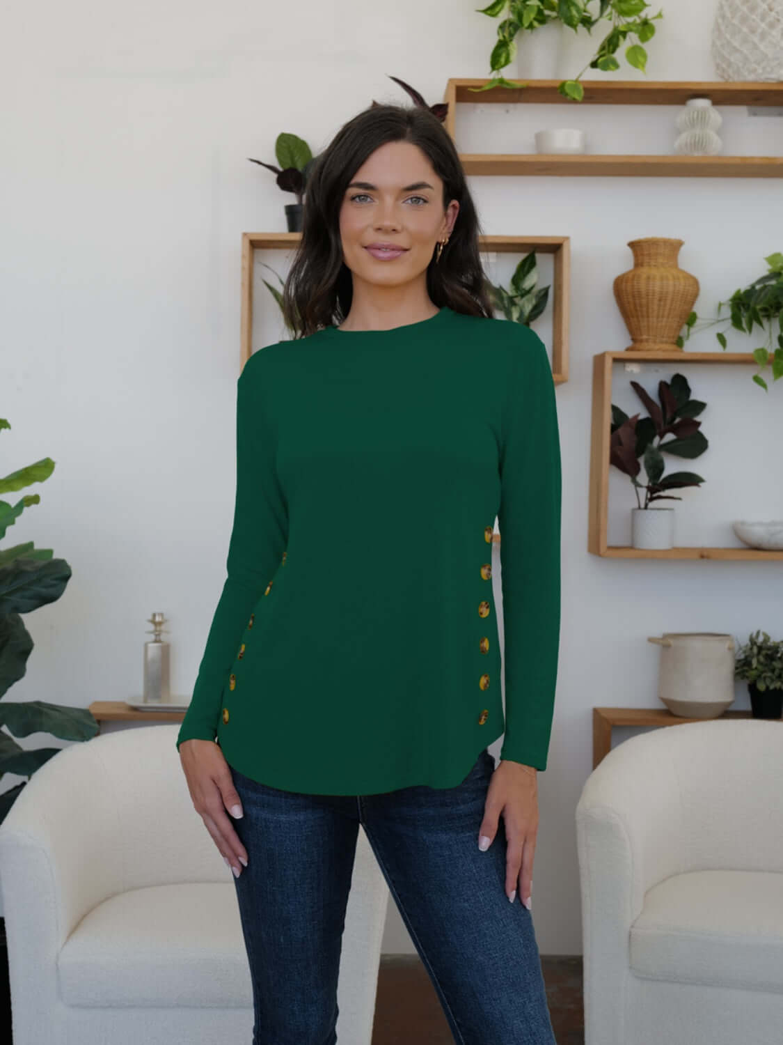 Woman in green FAM-FAM round neck long sleeve t-shirt with decorative buttons in a stylish room.