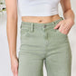 Woman wearing high-waisted raw hem wide-leg jeans in a soft green color, paired with a white crop top. Risen Jeans for a trendy look.