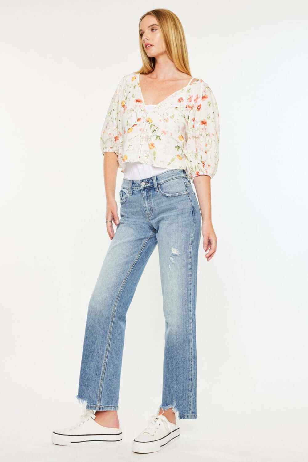 Woman wearing Kancan mid-rise frayed hem straight jeans in medium wash paired with a floral top, showcasing trendy, relaxed style.