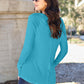 Woman wearing a turquoise round neck long sleeve t-shirt with jeans, standing outdoors.