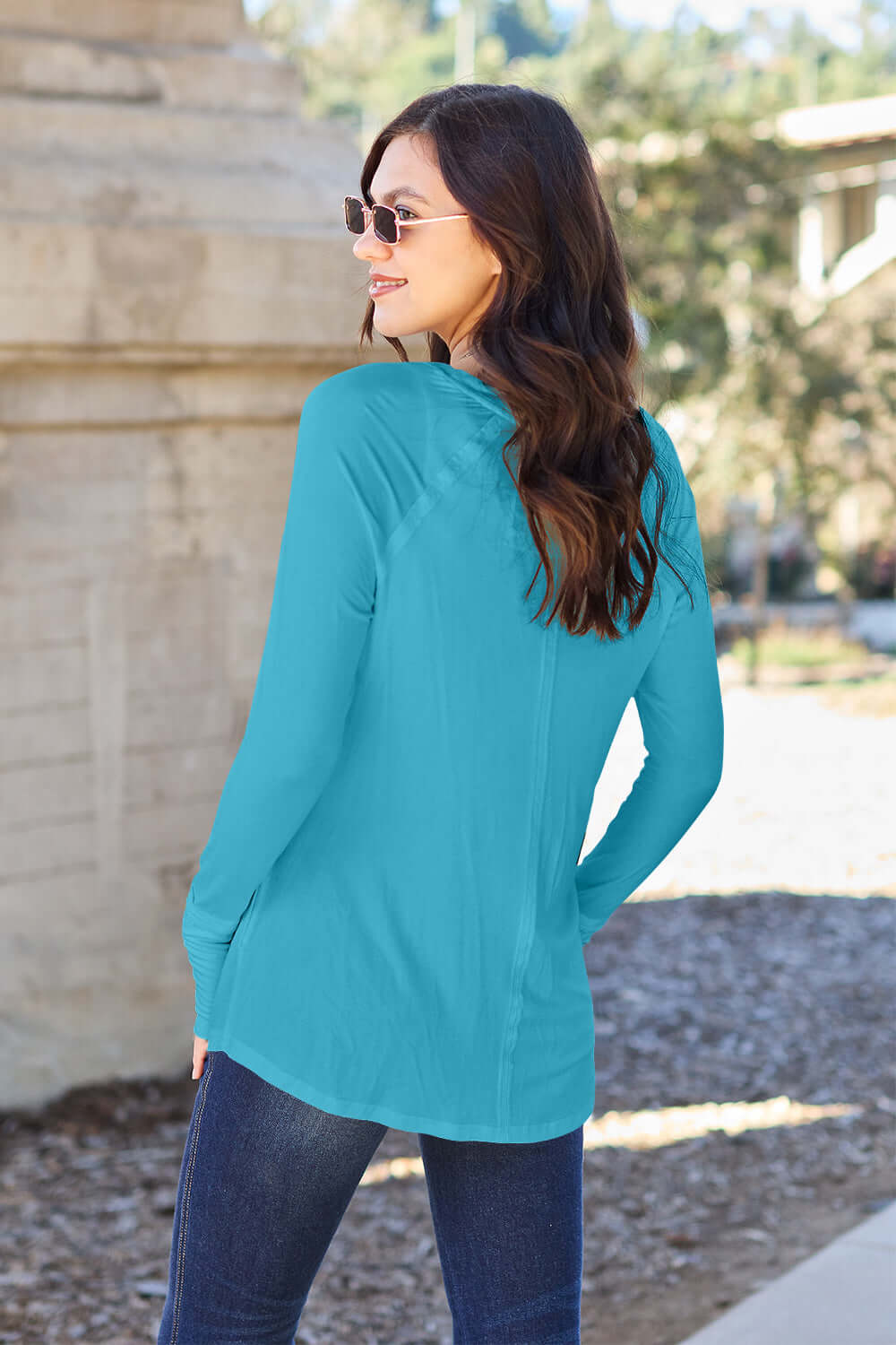 Woman wearing a turquoise round neck long sleeve t-shirt with jeans, standing outdoors.