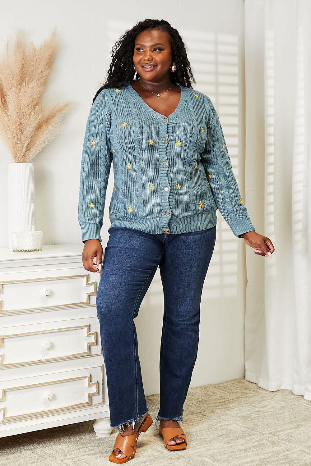 Woman wearing HEYSON floral embroidered cable cardigan in blue with jeans, showcasing cozy style and nature-inspired elegance.