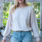 Woman in casual knit top and denim shorts standing outdoors.