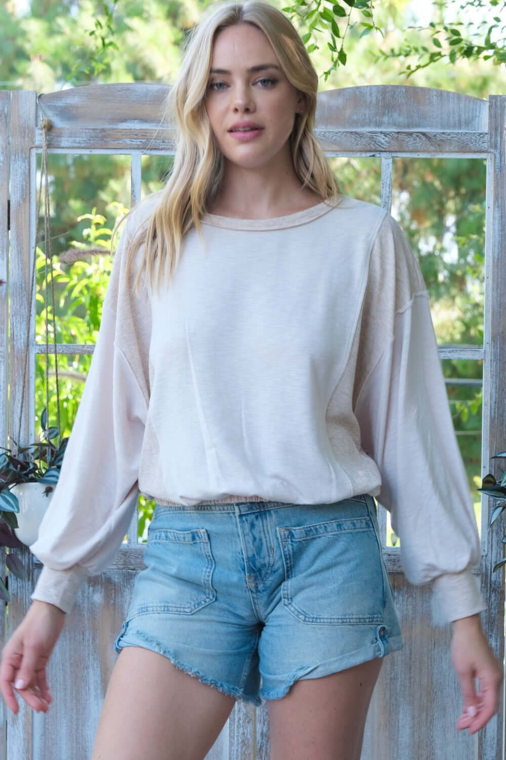 Woman in casual knit top and denim shorts standing outdoors.