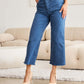 Woman wearing Crop Chloe Full Size Tummy Control High Waist Raw Hem Jeans by RFM Jeans, paired with beige heels in a stylish living room setting.