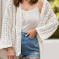 Woman wearing openwork open front dropped shoulder cardigan over white tank top and denim shorts.