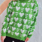 Woman wearing a green Bella Heart sweater with white heart contrast pattern and dropped shoulders for a cozy and chic look