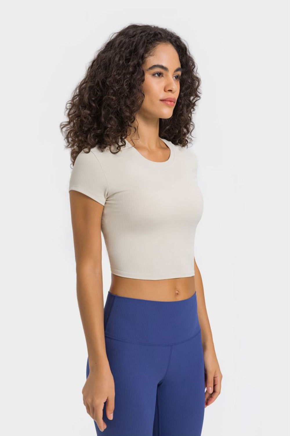 Model wearing the Millennia Round Neck Short Sleeve Cropped Sports T-Shirt in beige, styled with high-waisted leggings.